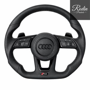 Könnte beinhalten: Schwarzes Lederlenkrad mit weißen Nähten, mit Audi-Logo und RS-Emblem. Das Lenkrad hat perforierte Bereiche und integrierte Bedienelemente. Das Rodin Products-Logo befindet sich in der oberen rechten Ecke.