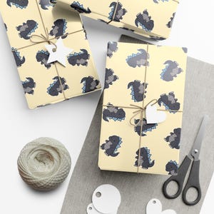 May include: Wrapping paper featuring a repeating pattern of cartoon monsters in dark gray with light blue dorsal fins on a pale yellow background. The paper is tied with twine and includes a white star-shaped gift tag on one of the packages.