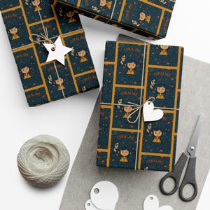 Op de afbeelding: Cadeaus verpakt met papier met een patroon met het woord "Coraline" en illustraties van een meisje en andere personages. De cadeaus zijn vastgebonden met touw en versierd met papieren uitsparingen. Een klosje touw en een schaar zijn ook aanwezig.