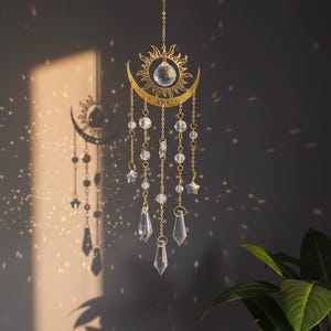 Può includere: Un acchiappasole a tema celeste con un design a forma di sole e luna crescente color oro. Perline di cristallo trasparente, stelle e pendenti a goccia pendono dal sole e dalla luna. L'acchiappasole è sospeso da una delicata catena.