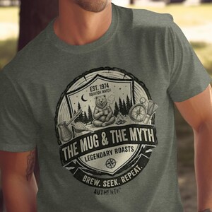 May include: Gray t-shirt featuring a circular graphic with a bear, trees, and camping elements. The text reads "THE MUG & THE MYTH LEGENDARY ROASTS" and "BREW. SEEK. REPEAT."