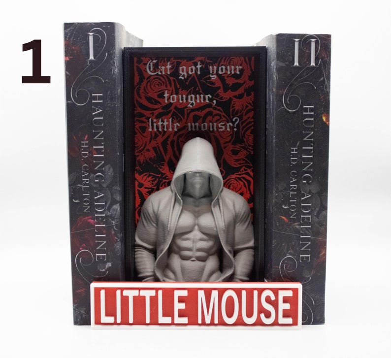 May include: A bookend set featuring two dark gray bookends with the text "HAUNTING ADELINE" and "HUNTING ADELINE". A central figure of a muscular person in a hooded jacket stands between the bookends. The base reads "LITTLE MOUSE".
