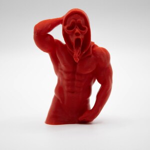 Puede incluir: Una figura roja y musculosa de la m&aacute;scara de Ghostface de la franquicia de pel&iacute;culas de terror Scream. La figura posa con un brazo levantado hacia la cabeza y el otro a un lado. La figura est&aacute; sobre un fondo blanco.