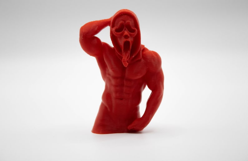 Puede incluir: Una figura roja y musculosa de la m&aacute;scara de Ghostface de la franquicia de pel&iacute;culas de terror Scream. La figura posa con un brazo levantado hacia la cabeza y el otro a un lado. La figura est&aacute; sobre un fondo blanco.