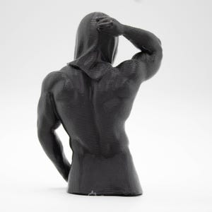 Puede incluir: Escultura gris oscuro de una figura musculosa, vista desde atr&aacute;s. La figura lleva una capucha y tiene un brazo levantado, tocando la cabeza. La escultura est&aacute; sobre un fondo blanco.