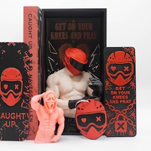 Könnte beinhalten: Ein Set bestehend aus einem Buch mit dem Titel CAUGHT UP, einer muskulösen Figur mit rotem Helm, einer pfirsichfarbenen Geistermasken-Figur, einem roten Helm-Schlüsselanhänger und zwei schwarzen Lesezeichen mit roten Grafiken und dem Text GET ON YOUR KNEES AND PRAY.