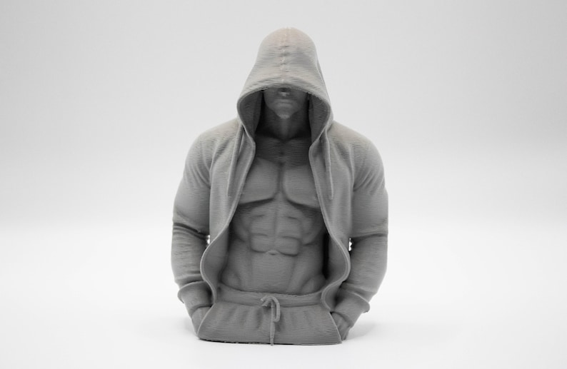 May include: A monochromatic gray 3D printed bust of a muscular torso wearing a hooded sweatshirt. The figure features a defined abdominal area, long sleeves, and a hood pulled over the head. The sweatshirt includes a front pocket and a drawstring.