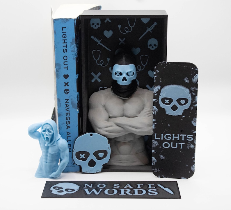 May include: A collection of novelty items featuring a skull theme. Includes a figurine of a muscular figure with a skull mask, a bookmark, a keychain, and a book with the text "LIGHTS OUT". The items are in shades of blue and black.