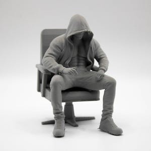 May include: A monochromatic gray 3D printed figurine of a muscular figure wearing a hooded sweatshirt and pants, seated in a high-backed office chair. The figure has a defined torso visible through the open hoodie and wears athletic-style shoes.