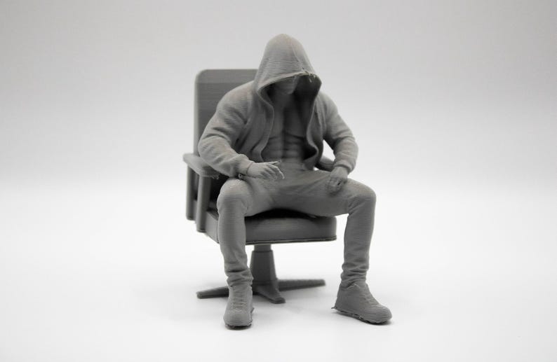 May include: A monochromatic gray 3D printed figurine of a muscular figure wearing a hooded sweatshirt and pants, seated in a high-backed office chair. The figure has a defined torso visible through the open hoodie and wears athletic-style shoes.