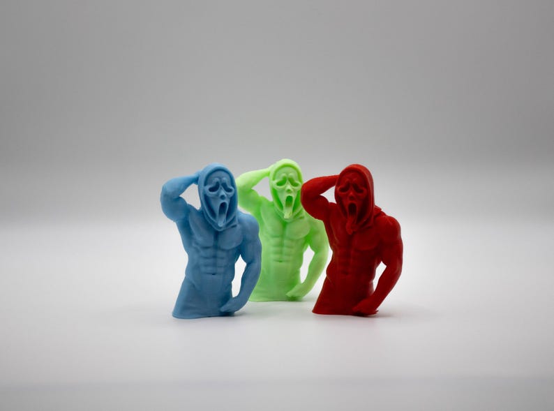 Puede incluir: Tres figuras coloridas del personaje de la m&aacute;scara de Scream. Las figuras son azules, verdes y rojas, cada una con un f&iacute;sico musculoso y una capucha. Las figuras posan con una mano en la cabeza.