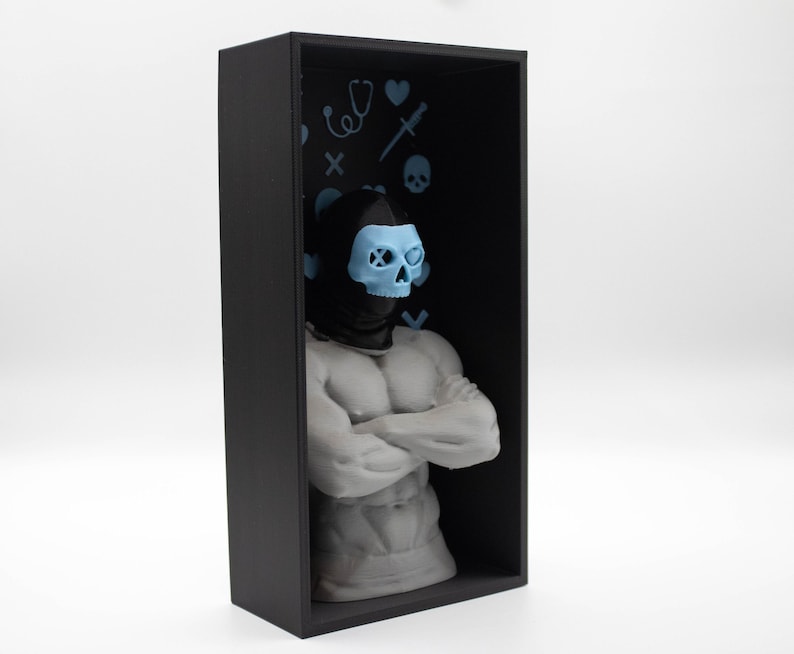 May include: A black rectangular display case houses a white muscular torso sculpture with arms crossed. The sculpture wears a black hood and a light blue skull mask. The case's black interior features light blue medical-themed icons.