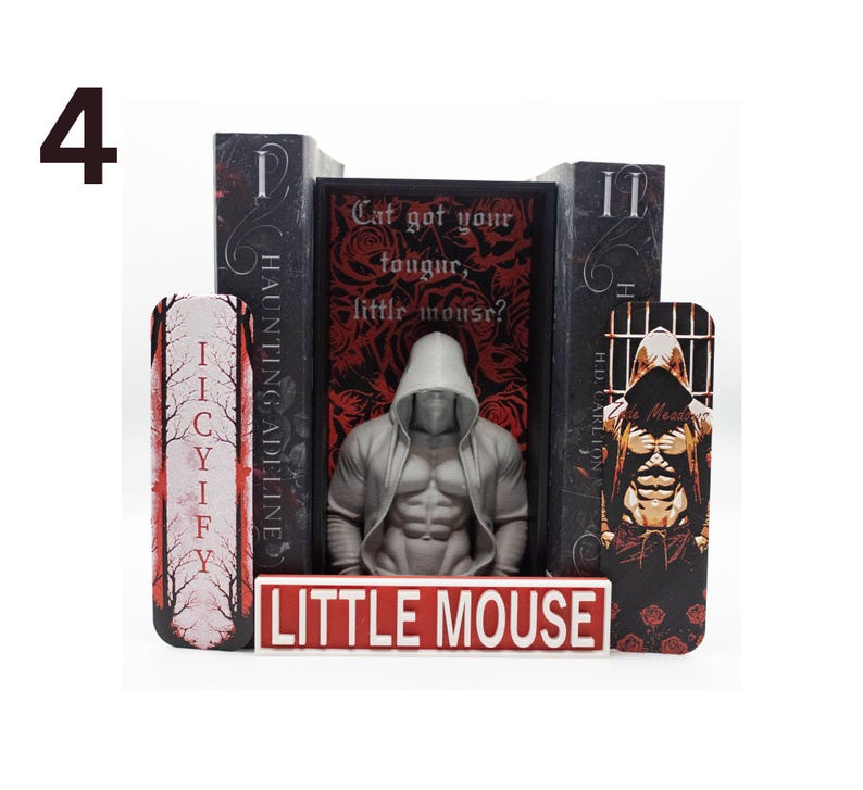 May include: A book display featuring a muscular, hooded figure statue, flanked by decorative bookends. The bookends have text that reads "IICYIFY" and "HAUNTING ADELINE". A sign at the base reads "LITTLE MOUSE". The central book has the text "Cat got your tougur, little mousr?"