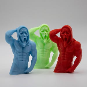 Puede incluir: Tres figuras coloridas del personaje de Ghostface de la serie de pel&iacute;culas de terror Scream. Las figuras son azules, verdes y rojas, cada una con una constituci&oacute;n muscular y la ic&oacute;nica m&aacute;scara. Las figuras posan con una mano en la cabeza.