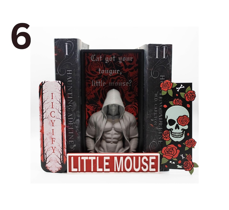 May include: A display featuring a hooded figure statue, books, and decorative elements. The books have titles like "Haunting Adeline" and "Cat got your tongue, little mouse?" A sign reads "Little Mouse". The color scheme is black, red, and white.