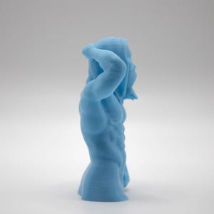 Puede incluir: Una escultura azul claro de una figura masculina musculosa, con un brazo levantado por encima de la cabeza. La figura tiene m&uacute;sculos abdominales definidos y est&aacute; de pie en una pose relajada. La escultura est&aacute; sobre un fondo blanco.
