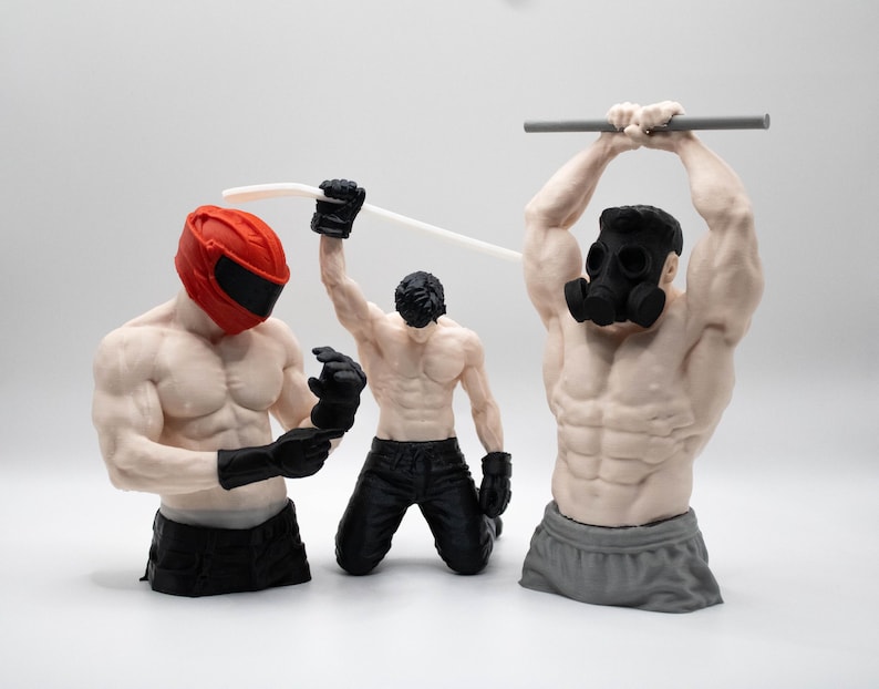 May include: Three muscular male figurines. The left figure wears a red helmet and black gloves. The center figure kneels, wearing black pants and gloves, holding a white hockey stick. The right figure wears a black gas mask and grey shorts.
