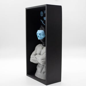 May include: A black rectangular shadow box contains a gray statue of a muscular figure with arms crossed. A light blue skull mask is on the figure's face. Light blue skull and crossbones, heart, and knife icons are on the back wall.