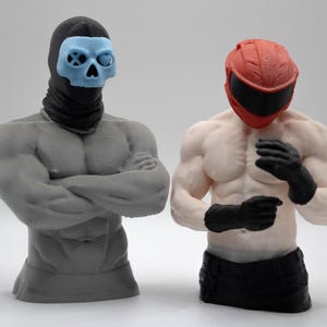 May include: Two muscular torso figurines. The left figure is gray with a black balaclava and a light blue skull mask. The right figure is skin-toned with a red motorcycle helmet and black gloves, wearing black pants. Both are standing upright.