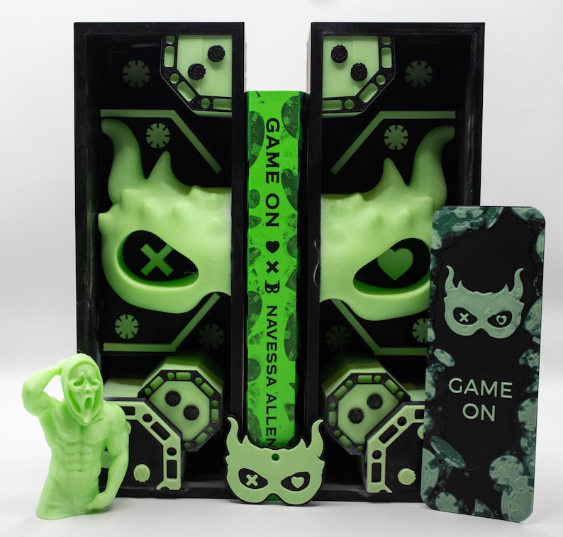 May include: A neon green and black display featuring a book with the title "Game On" and the author's name, Navessa Allen. The display includes a figurine, a mask, and a decorative panel with a mask design. The overall theme is a horror-themed book.