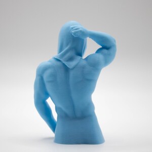 Puede incluir: Escultura azul claro de una figura musculosa con capucha, vista desde atr&aacute;s. El brazo derecho de la figura est&aacute; levantado, la mano toca la cabeza. La escultura est&aacute; sobre un fondo blanco.