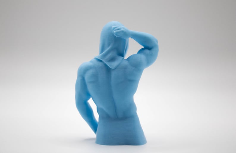 Puede incluir: Escultura azul claro de una figura musculosa con capucha, vista desde atr&aacute;s. El brazo derecho de la figura est&aacute; levantado, la mano toca la cabeza. La escultura est&aacute; sobre un fondo blanco.