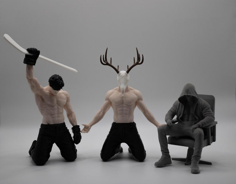 May include: Three figurines: one kneeling figure holding a white hockey stick, a central kneeling figure with a deer skull head and antlers, and a third figure in a hooded sweatshirt sitting on a chair, all featuring detailed muscular anatomy.