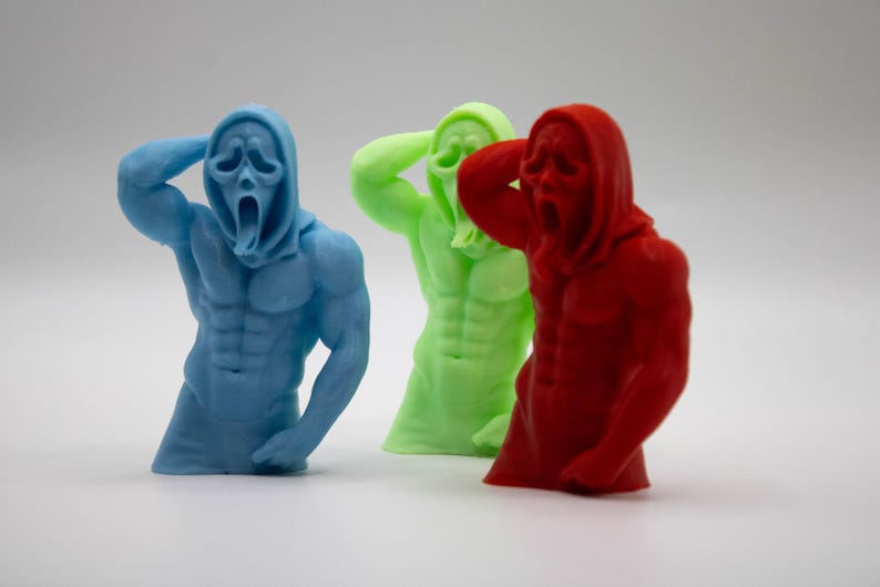 Puede incluir: Tres esculturas coloridas de una figura musculosa con una m&aacute;scara de Scream. Las figuras son azules, verdes y rojas. Las figuras tienen una capucha y est&aacute;n esculpidas con abdominales y brazos definidos.