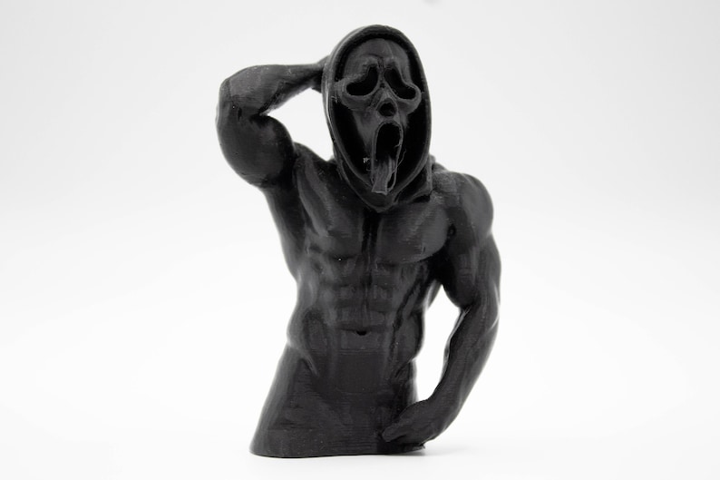 Puede incluir: Escultura negra de una figura musculosa con una m&aacute;scara de Scream. La figura posa con un brazo levantado hacia la cabeza, mostrando m&uacute;sculos definidos y una expresi&oacute;n facial detallada. La escultura est&aacute; sobre un fondo blanco.