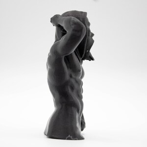 Puede incluir: Escultura gris oscuro de una figura musculosa, parcialmente cubierta. La figura est&aacute; en una pose din&aacute;mica, con un brazo levantado, la tela drapeada sobre la cabeza. La escultura tiene una superficie texturizada, sobre fondo blanco.