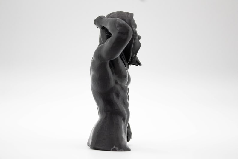 Puede incluir: Escultura gris oscuro de una figura musculosa, parcialmente cubierta. La figura est&aacute; en una pose din&aacute;mica, con un brazo levantado, la tela drapeada sobre la cabeza. La escultura tiene una superficie texturizada, sobre fondo blanco.