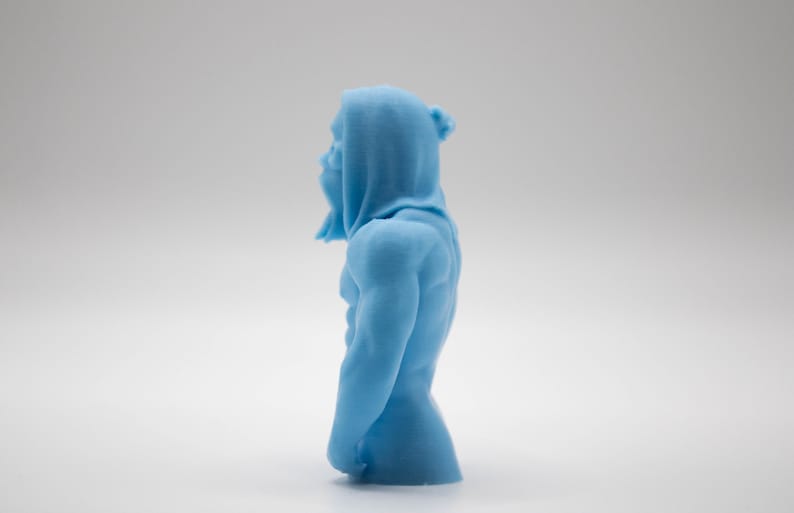 Puede incluir: Una figura azul claro de una figura musculosa con capucha. La escultura es detallada, mostrando la forma del cuerpo y la textura de la tela. La figura est&aacute; de pie en una pose relajada.