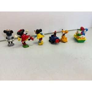 K&ouml;nnte beinhalten: Eine Sammlung kleiner, farbenfroher Disney-Charakterfiguren. Das Set enth&auml;lt Minnie Mouse, Mickey Mouse, Pluto, Donald Duck und einen Miniaturzug. Die Figuren sind aus Kunststoff und in verschiedenen Posen.
