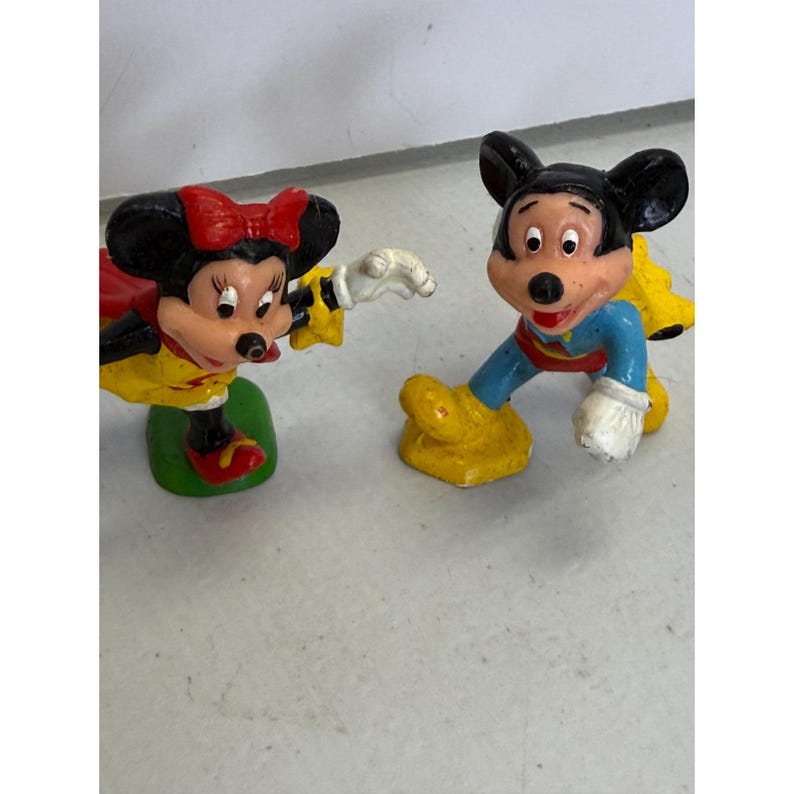 K&ouml;nnte beinhalten: Zwei kleine Figuren von Zeichentrickfiguren. Eine ist eine weibliche Maus mit roter Schleife, gelber Jacke und roten Schuhen. Die andere ist eine m&auml;nnliche Maus in blauer und gelber Kleidung. Beide sind in einer spielerischen Pose.