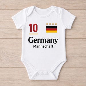 May include: White baby bodysuit with the number 10 in red, the word "Germany" in black, and the word "Mannschaft" below it. The German flag and four gold stars are printed on the upper right. The bodysuit has snap closures.