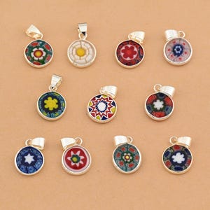 May include: A collection of round, colorful glass pendant necklaces with silver-tone metal bails. The pendants feature intricate floral and geometric designs in various colors, including red, blue, yellow, and green. The pendants are displayed on a light brown surface.