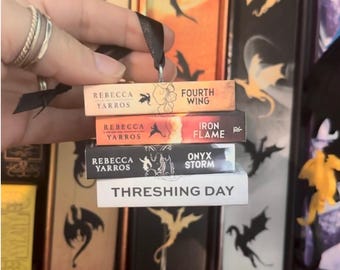 May include: A miniature book ornament stack featuring four rectangular blocks with black ribbon. The spines are labeled Fourth Wing, Iron Flame, Onyx Storm, and Threshing Day, all authored by Rebecca Yarros, with dragon silhouettes and text.
