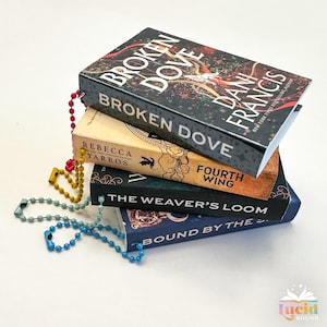 May include: A stack of four books with colorful covers and beaded bookmarks. The top book is titled "Broken Dove" by Dani Francis. The second book is titled "Broken Dove" by Rebecca Yarros. The third book is titled "Fourth Wing". The bottom book is titled "Bound by the..."