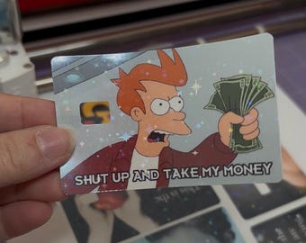 May include: A rectangular card featuring a holographic finish with a cartoon character with orange hair holding a fan of green paper money. The text SHUT UP AND TAKE MY MONEY is printed in black capital letters at the bottom of the card.