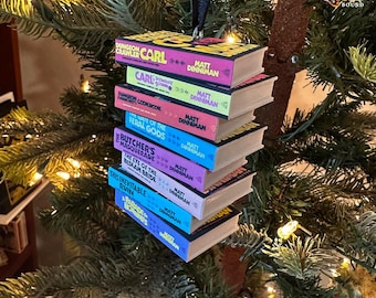 May include: A miniature stack of seven Dungeon Crawler Carl books by Matt Dinniman, including titles like The Butcher's Masquerade and The Eye of the Bedlam Bride, hanging as a decorative ornament with a black ribbon loop.
