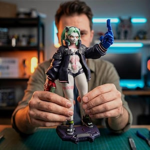 May include: A detailed figurine of a female character with green hair, red eyes, and a futuristic outfit. The figure is wearing a black jacket, white and black undergarments, and a blue glove. The figure is standing on a purple base.