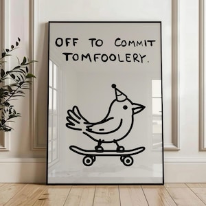 May include: Framed art print featuring the text "OFF TO COMMIT TOMFOOLERY." The image shows a black and white illustration of a bird wearing a party hat and riding a skateboard. The print is displayed on a white wall.
