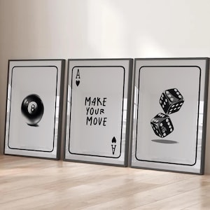 Pode incluir: Três impressões emolduradas com ilustrações temáticas de jogos. Uma impressão mostra uma bola preta número 8, outra um Ás de copas com o texto "MAKE YOUR MOVE", e a terceira, dois dados pretos. Todas as impressões têm fundo branco.