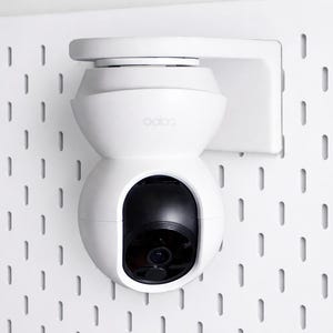 Op de afbeelding: Een witte beveiligingscamera gemonteerd op een wit pegboard. De camera heeft een afgerond ontwerp met een zwarte lens en de merknaam "aoion" aan de zijkant. Het pegboard heeft een reeks gelijkmatig verdeelde rechthoekige gaten.