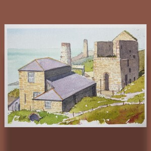 Peut inclure: Peinture à l'aquarelle d'un paysage côtier avec des bâtiments en pierre et des cheminées. Les bâtiments ont des toits gris et sont situés sur une colline herbeuse surplombant la mer. L'œuvre est encadrée en blanc.