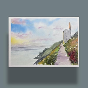 Puede incluir: Pintura a la acuarela de un paisaje costero. Un camino conduce a un edificio de piedra con una chimenea en una ladera. El cielo es una mezcla de azul, amarillo y rosa. Plantas verdes y rojas bordean el camino, con el mar al fondo.