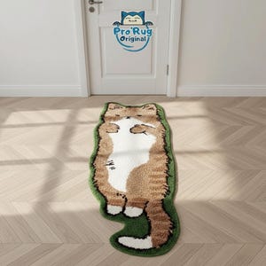 Könnte beinhalten: Ein braun-weißes Katzen-förmiger Teppich mit grünem Rand liegt auf einem Holzboden. Der Teppich hat ein cartoonartiges Design, mit der Katze auf dem Rücken liegend. Im Hintergrund befindet sich eine weiße Tür mit einem Logo mit der Aufschrift "Pro Rug Original".