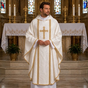 May include: A cream-colored liturgical chasuble featuring a gold embroidered cross on the center panel. The garment has a subtle tonal damask pattern, gold trim along the vertical panels and hem, and a high collar, worn over a white alb.