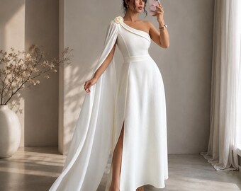 May include: A floor-length white gown featuring a single shoulder strap adorned with a fabric flower, a long flowing cape sleeve attached to the shoulder, a fitted bodice, and a high side slit that extends from the waist to the hemline.