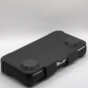 May include: A black smartphone case with two circular buttons on the top. The case has a textured surface and a rectangular shape. The phone case is designed to protect the phone.